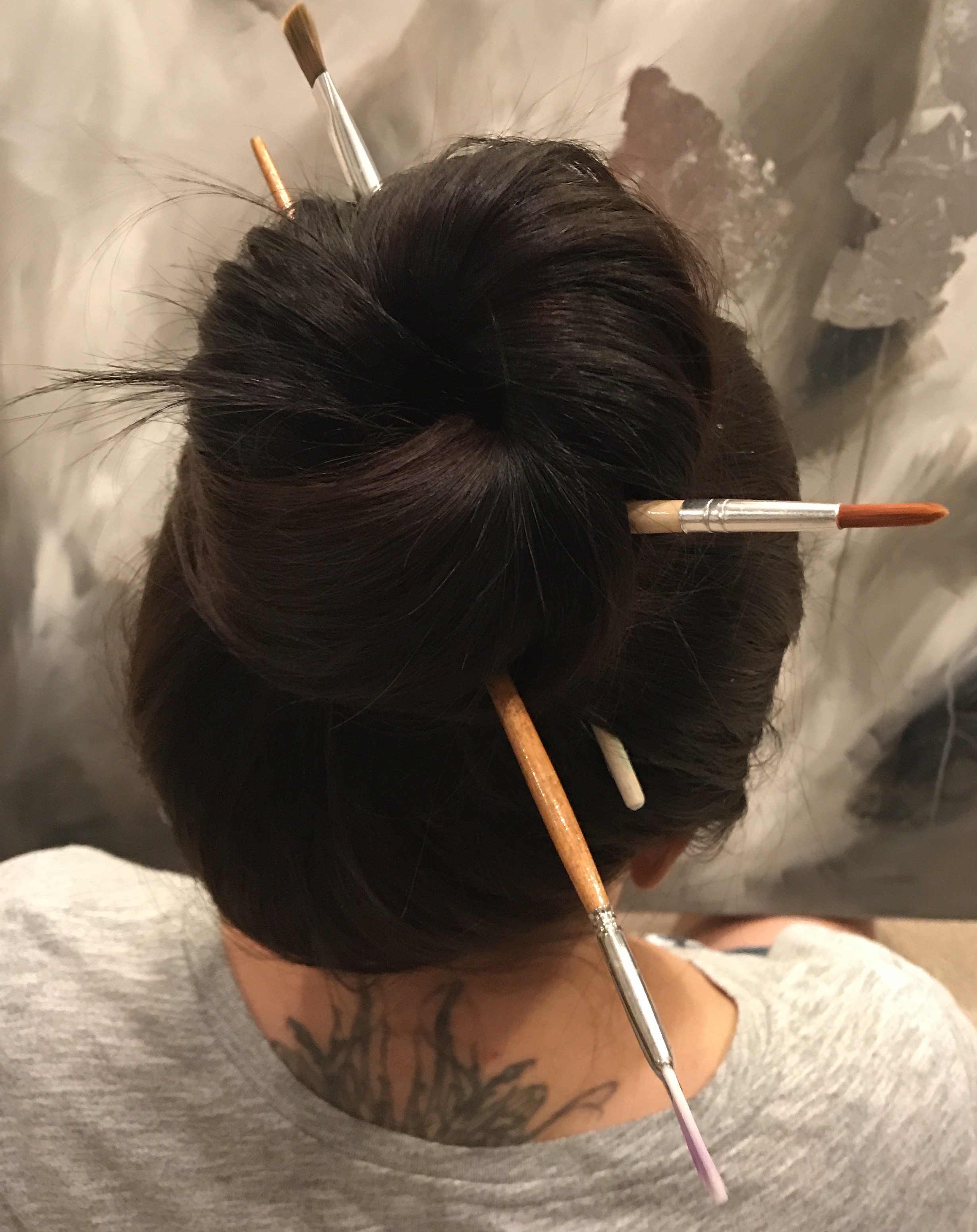 Molly with paintbrushes in her hair, painting in the background